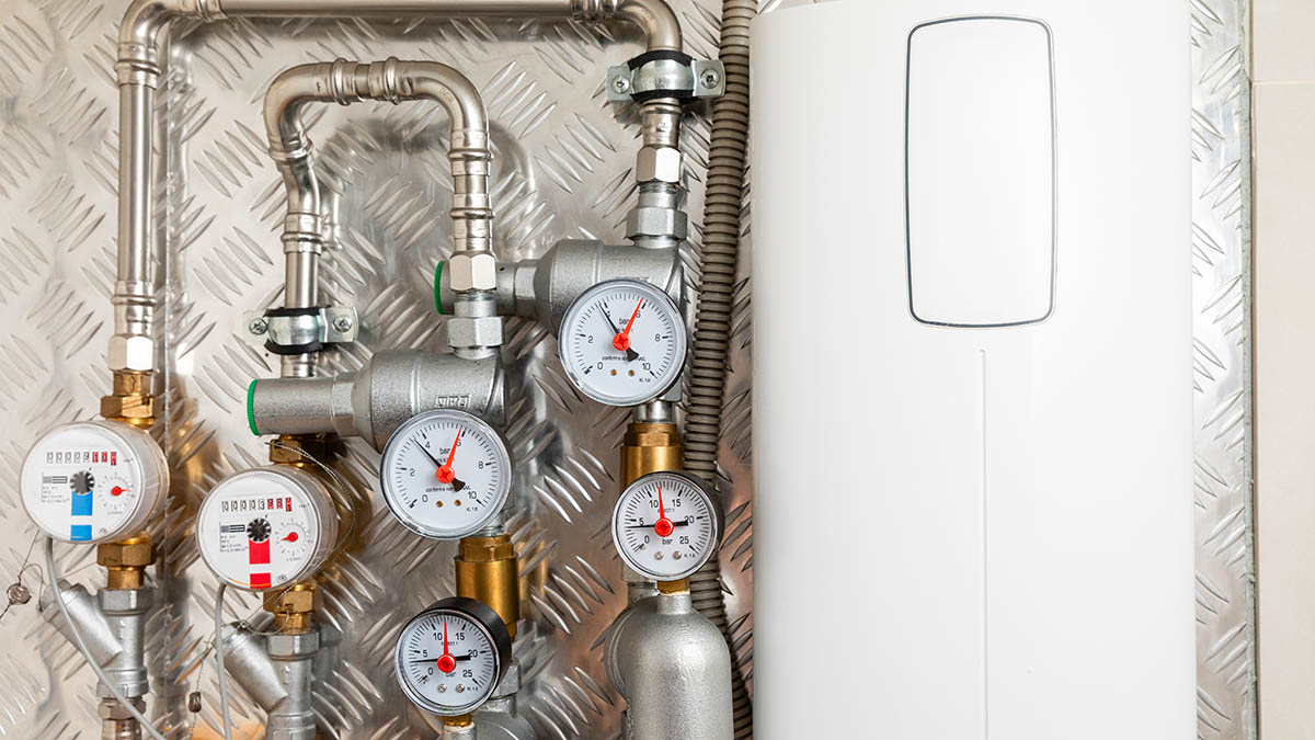 Water heating system with pressure gauges and pipes mounted on a metallic wall, featuring a modern white boiler unit for efficient heating solutions
